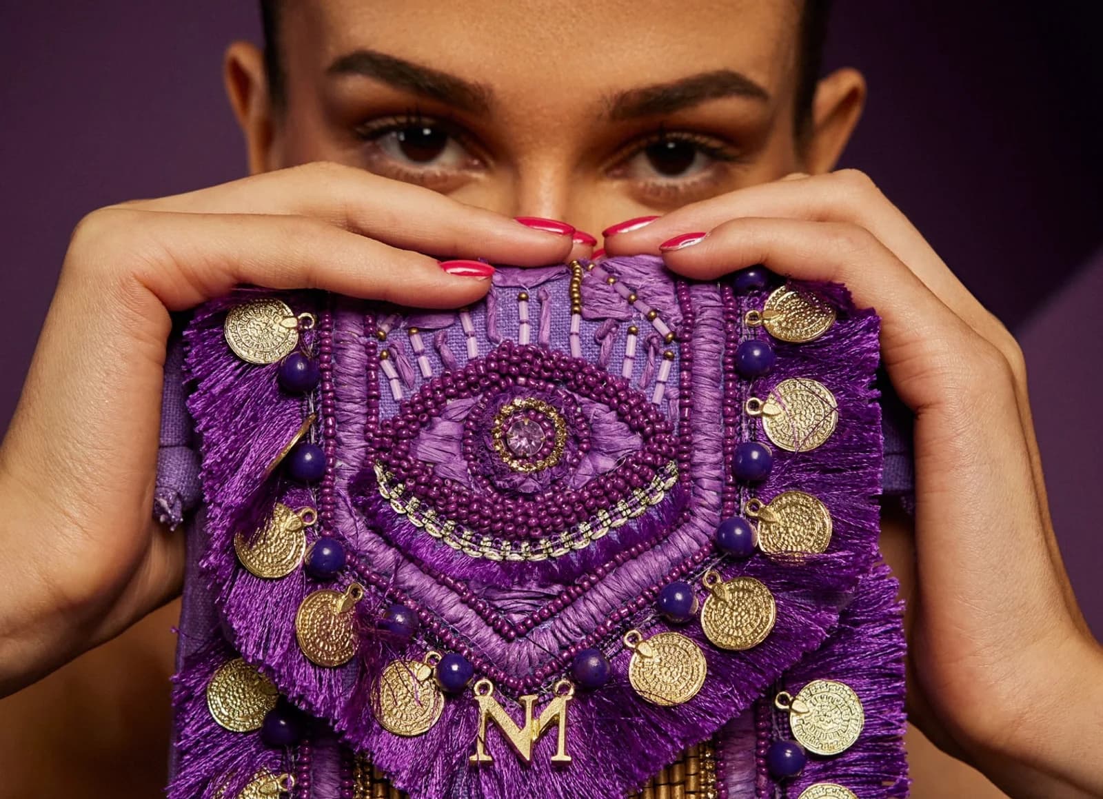 Hand-embroidered evil-eye bag in purple, held up to the face